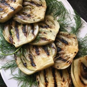 Grilled fennel placed over fennel fronds in a white platter. Grilled fennel is the perfect vegetable to be part of your grilled vegetable platter