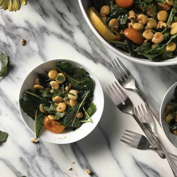 A small white salad bowl with lupini beans, baby kale and cherry tomatoes.