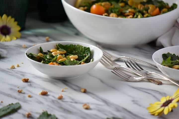 Scattered walnuts and kale leaves around a bowl of lupini salad.