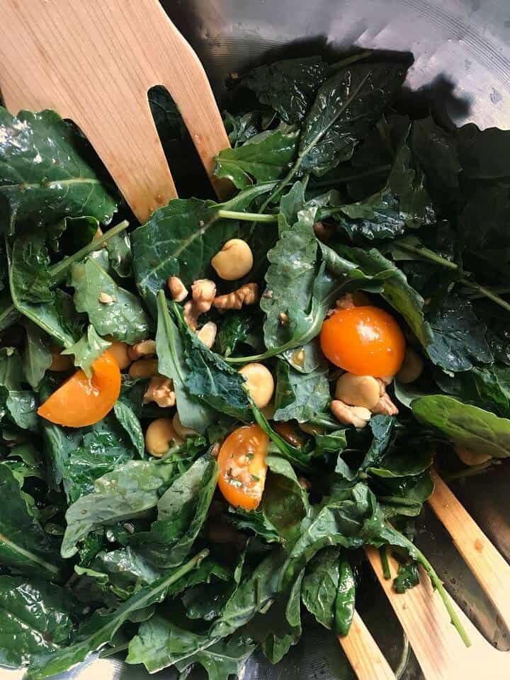 Lupini and kale being tossed together in a large salad bowl.