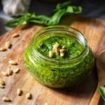 A jar of basil pesto set on a wooden board.