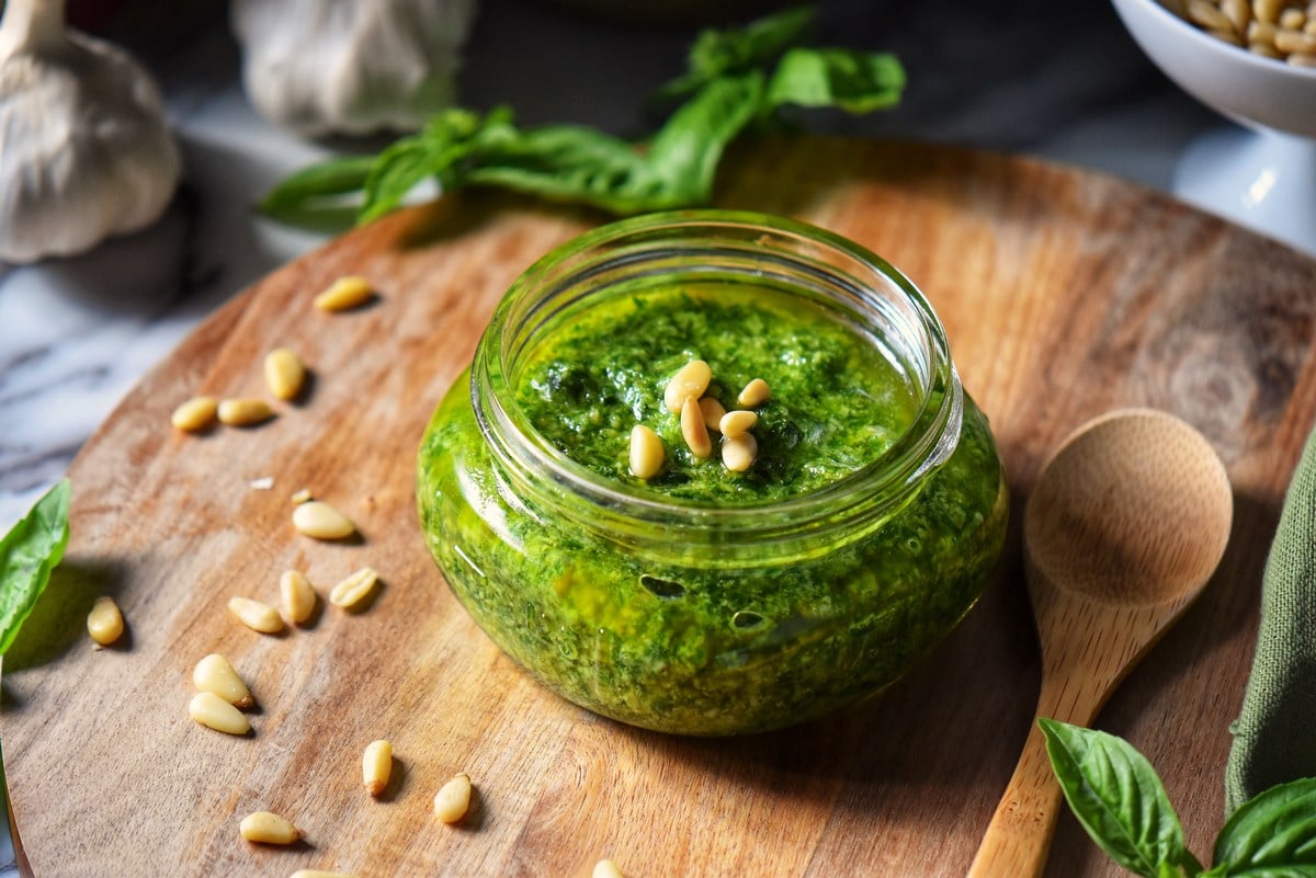 A jar of basil pesto set on a wooden board.