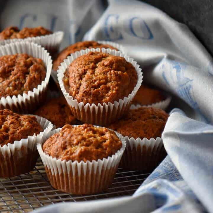 Banana muffins placed on a cooling rack, surrounded by a blue tea towel.