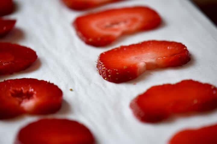 Sliced strawberries placed on a parchment lined baking tray.