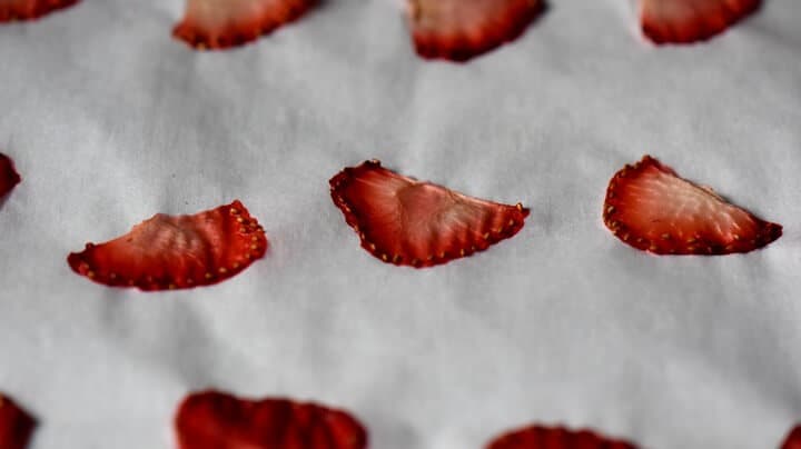 Visibility dehydrated strawberries on a parchment lined baking sheet. 