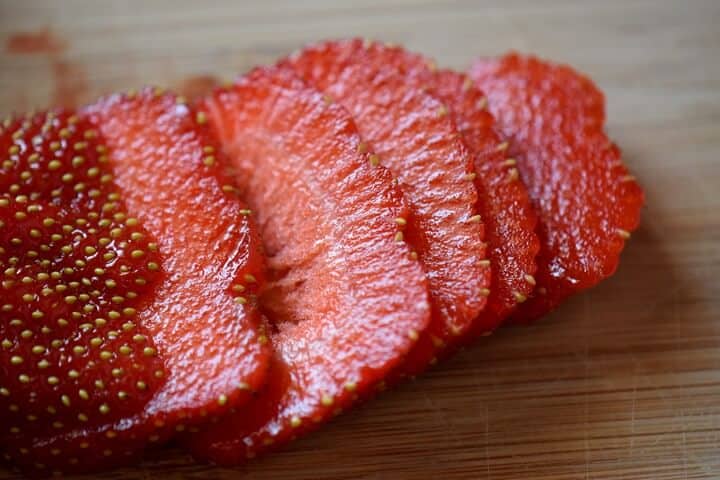A sliced strawberry on a wooden board.