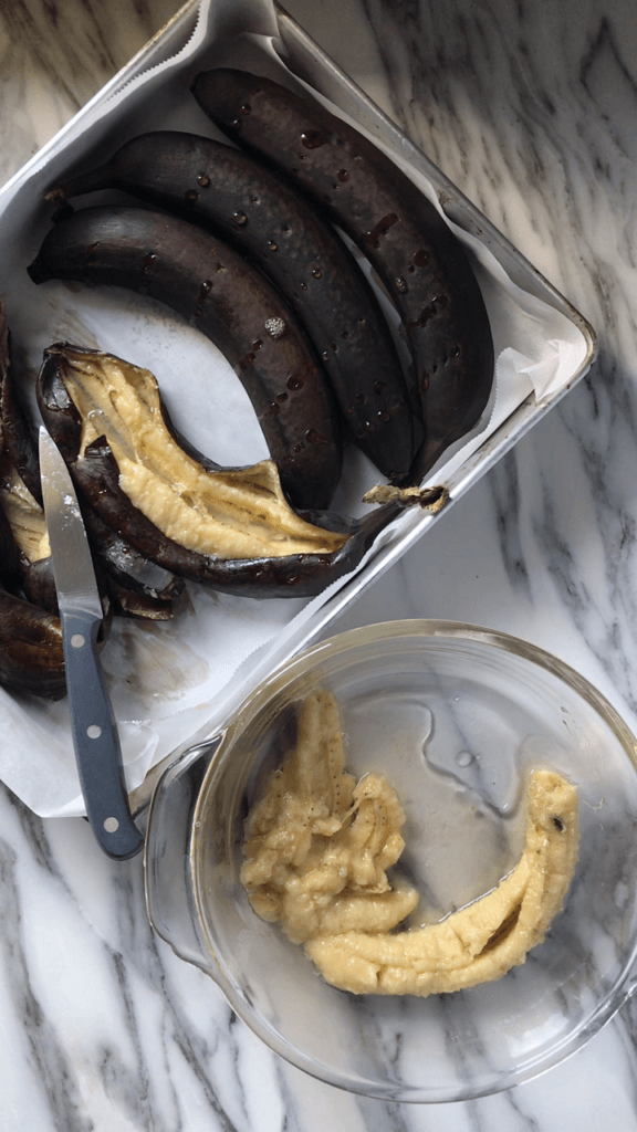 An overhead shot of Roasted Bananas in the process of being sliced open with a knife and transferred to a bowl. 