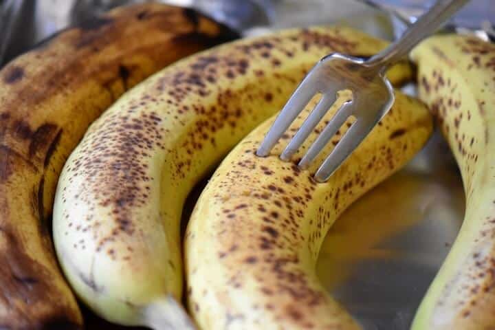 A fork piercing the outer skin of a ripe banana.