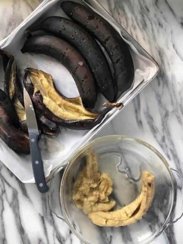 A few black bananas have been slit open with a knife. The interior of the roasted bananas are placed in a bowl.