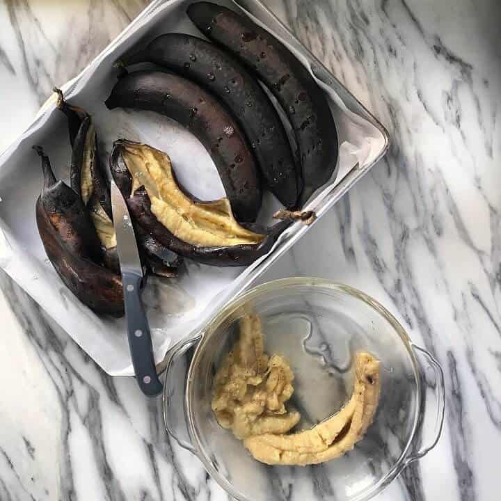A few black bananas have been slit open with a knife. The interior of the roasted bananas are placed in a bowl. 