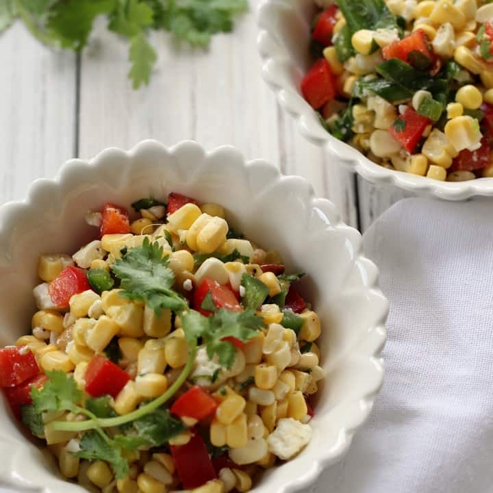 A close up shot of a white bowl filled with sweet corn salad.