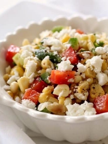 A white serving bowl of sweet corn salad sprinkled with feta cheese.