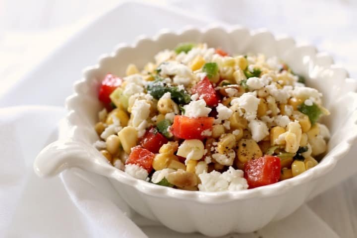 A white serving bowl of sweet corn salad sprinkled with feta cheese.