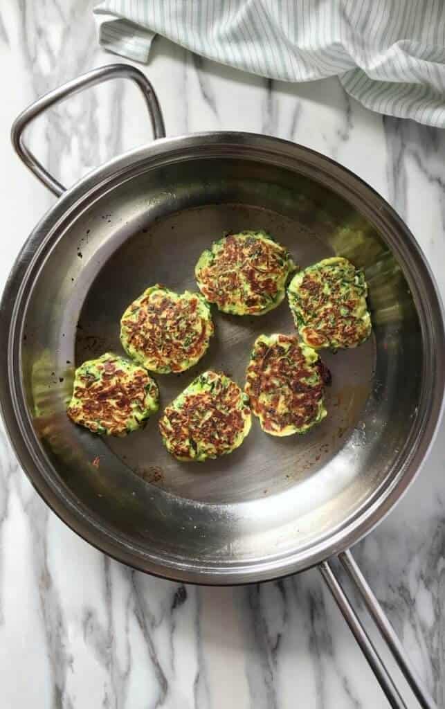 A heavy bottomed pan with six golden brown zucchini fritters.
