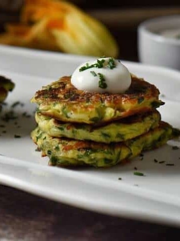 Vegetable fritters are stacked in groups of threes and are topped with a dollop of yogurt and sprinkled with chives.