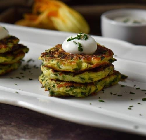 Vegetable fritters are stacked in groups of threes and are topped with a dollop of yogurt and sprinkled with chives.