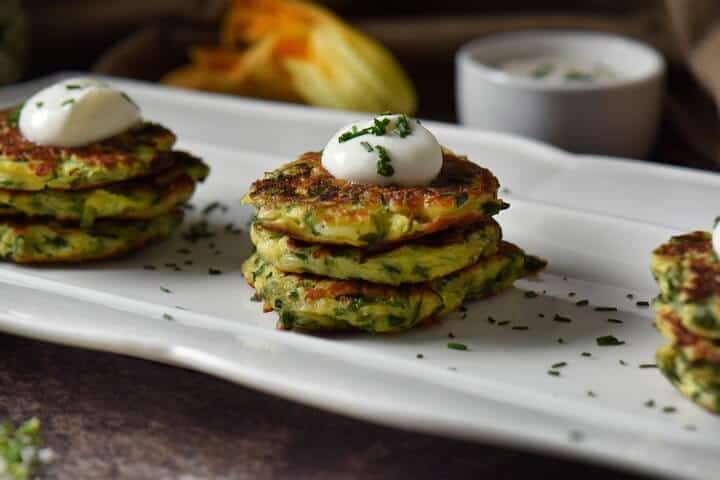 Vegetable fritters are stacked in groups of threes and are topped with a dollop of yogurt and sprinkled with chives.