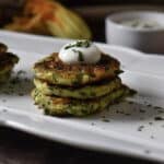 A stack of three zucchini cakes topped with yogurt on a white serving dish,