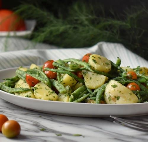 Italian potato salad with green beans and potatoes in a white serving platter.