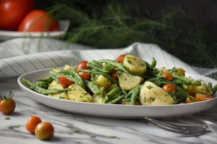 Italienischer Kartoffelsalat mit grünen Bohnen und Kartoffeln in einer weißen Servierplatte.