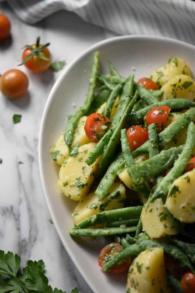 An overhead shot of the Italian Potato Salad in a white serving bowl surrounded by cherry tomatoes and parsley.