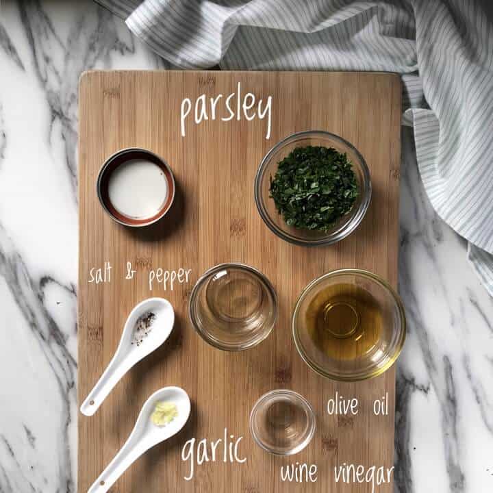 The ingredients used to make the parsley vinaigrette are measures and placed on a wooden board, ready to be mixed together.