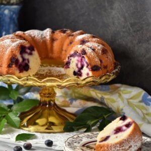 Lemon Blueberry Cake on a cake stand next to a slice of blueberry cake.