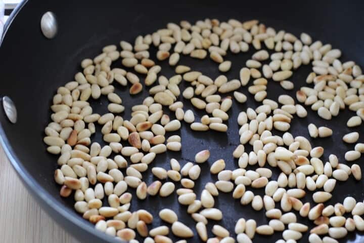 Pine nuts in the process of being toasted in a skillet.
