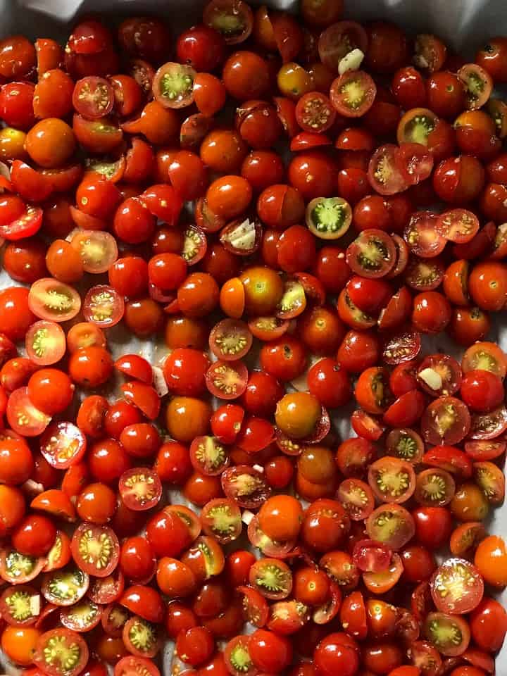 A baking sheet which had been lined with parchment paper is covered with sliced cherry tomatoes.
