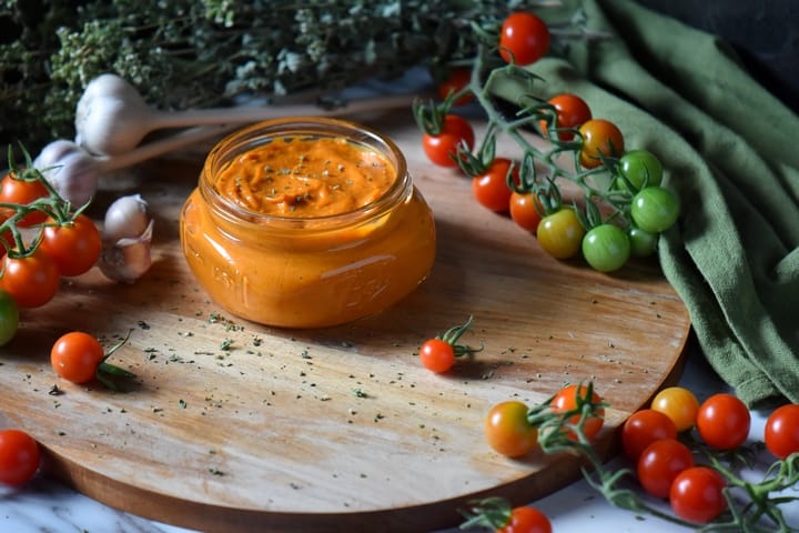 A jar of cherry tomato sauce surrounded by cherry tomatoes on a vine.