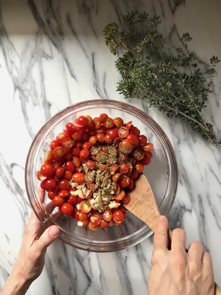 Sliced garlic and dried oregano in the process of being mixed with the sliced cherry tomatoes.