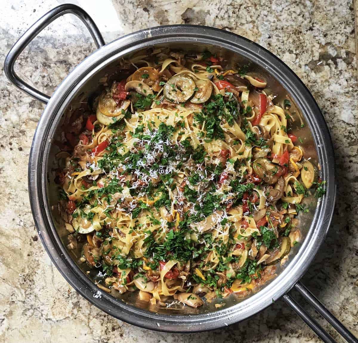 The grilled vegetable pasta is in the pan and has been topped with cheese and parsley. 