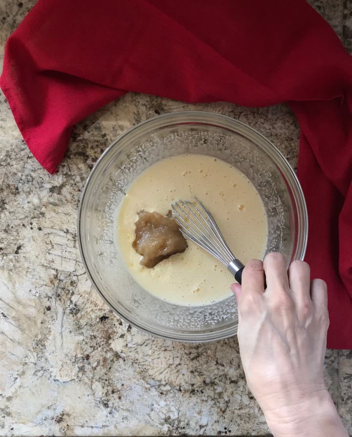 Homemade applesauce is being added to the wet ingredients of the apple cake.