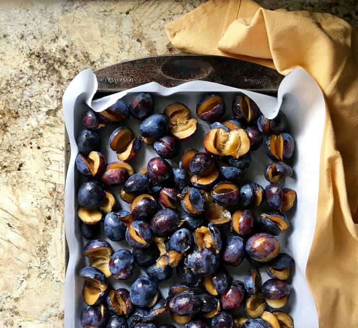 A large baking pan with sliced prunes about to be roasted.