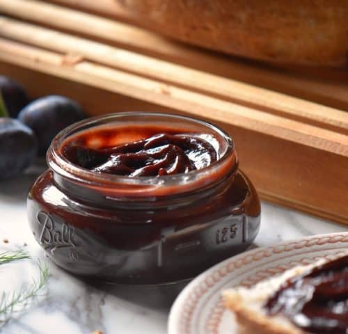 A jar of plum butter surrounded by fresh prune plums.