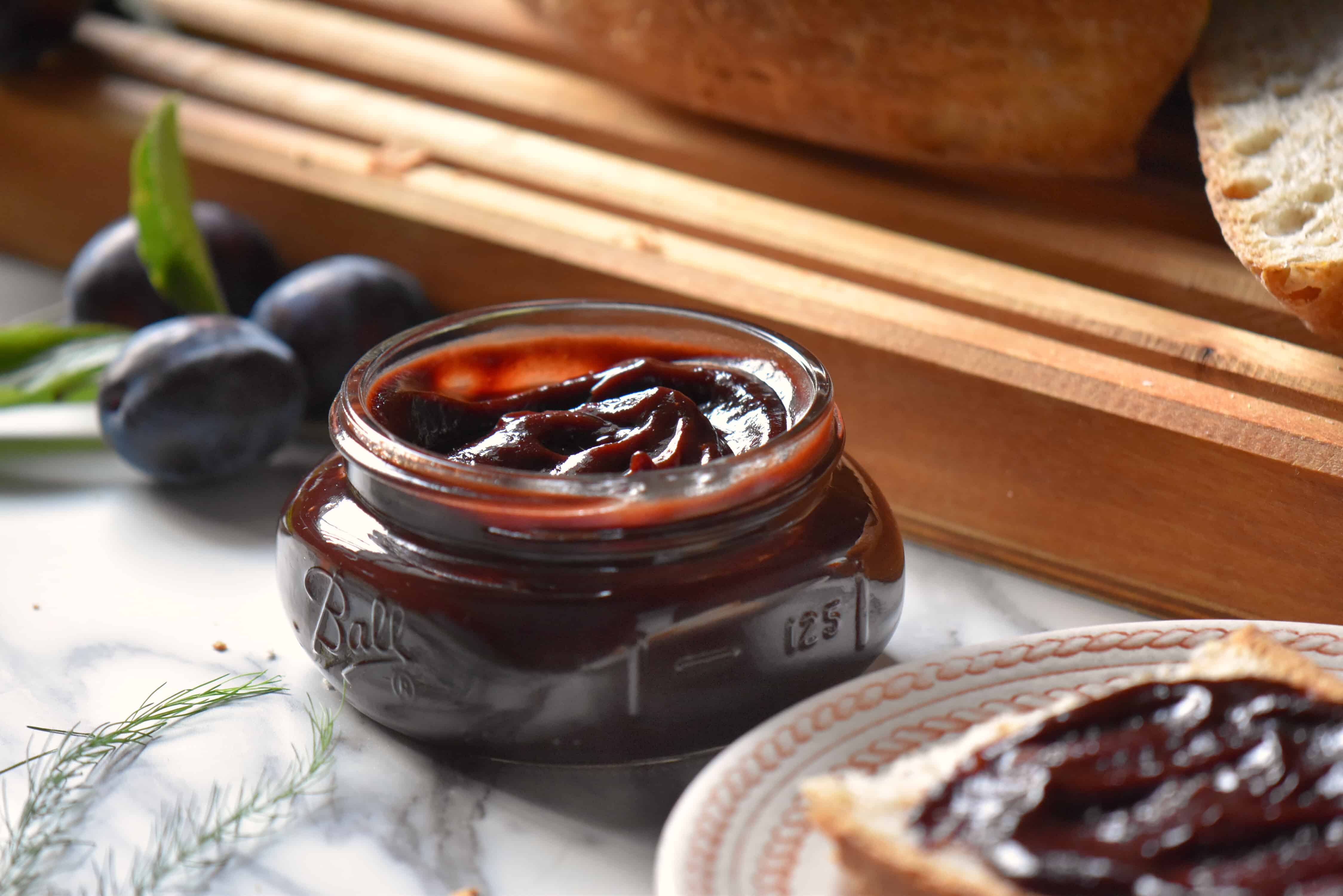 A jar of plum butter surrounded by fresh prune plums.