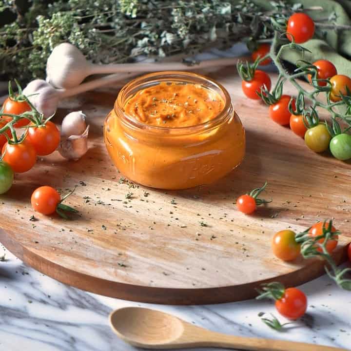Roasted Cherry Tomato Sauce in a jar, surrounded by fresh garlic, fresh cherry tomatoes and dried oregano.