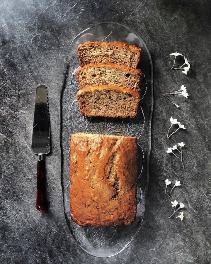 An overhead shot of a sliced banana bread on a glass serving tray.