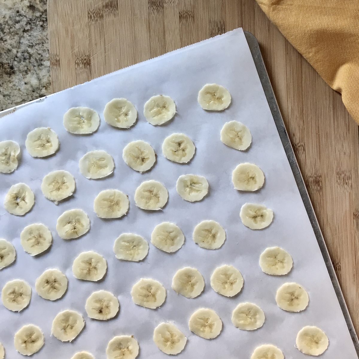 Thinly sliced bananas on a parchment lined baking sheet.