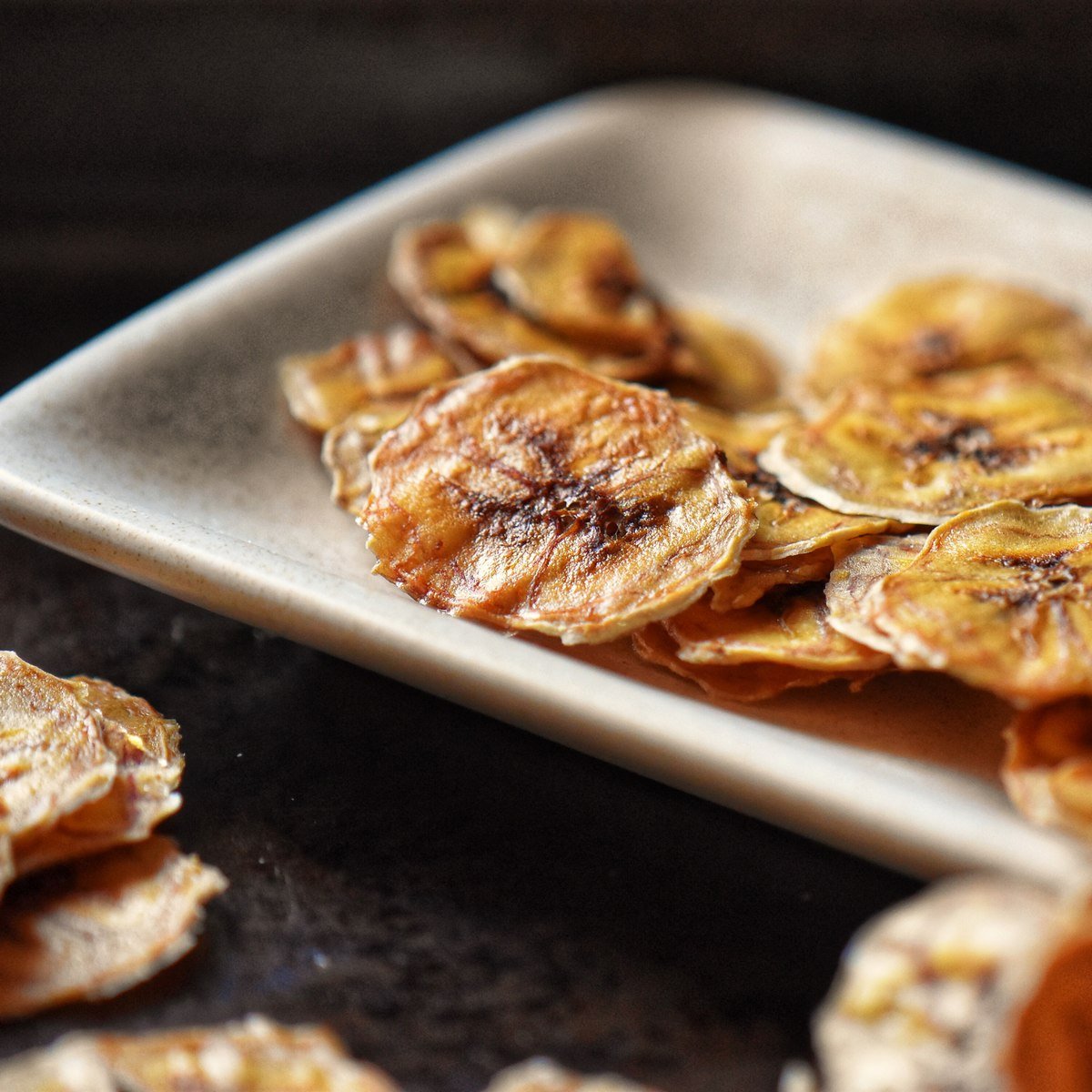 Baked banana chips placed on a white serving dish.