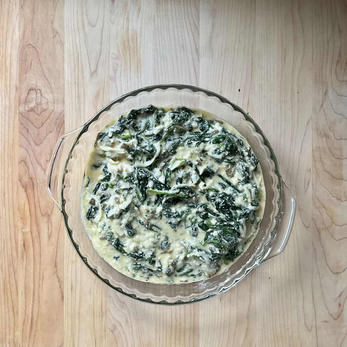 The spinach, egg and cheese filling for a crustless quiche in a pan.