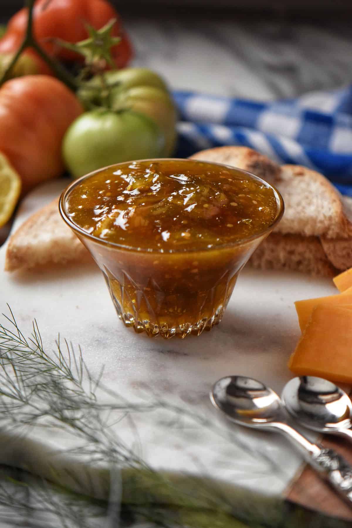 A close up of tomato jam on a marble board surrounded by cheese and bread.