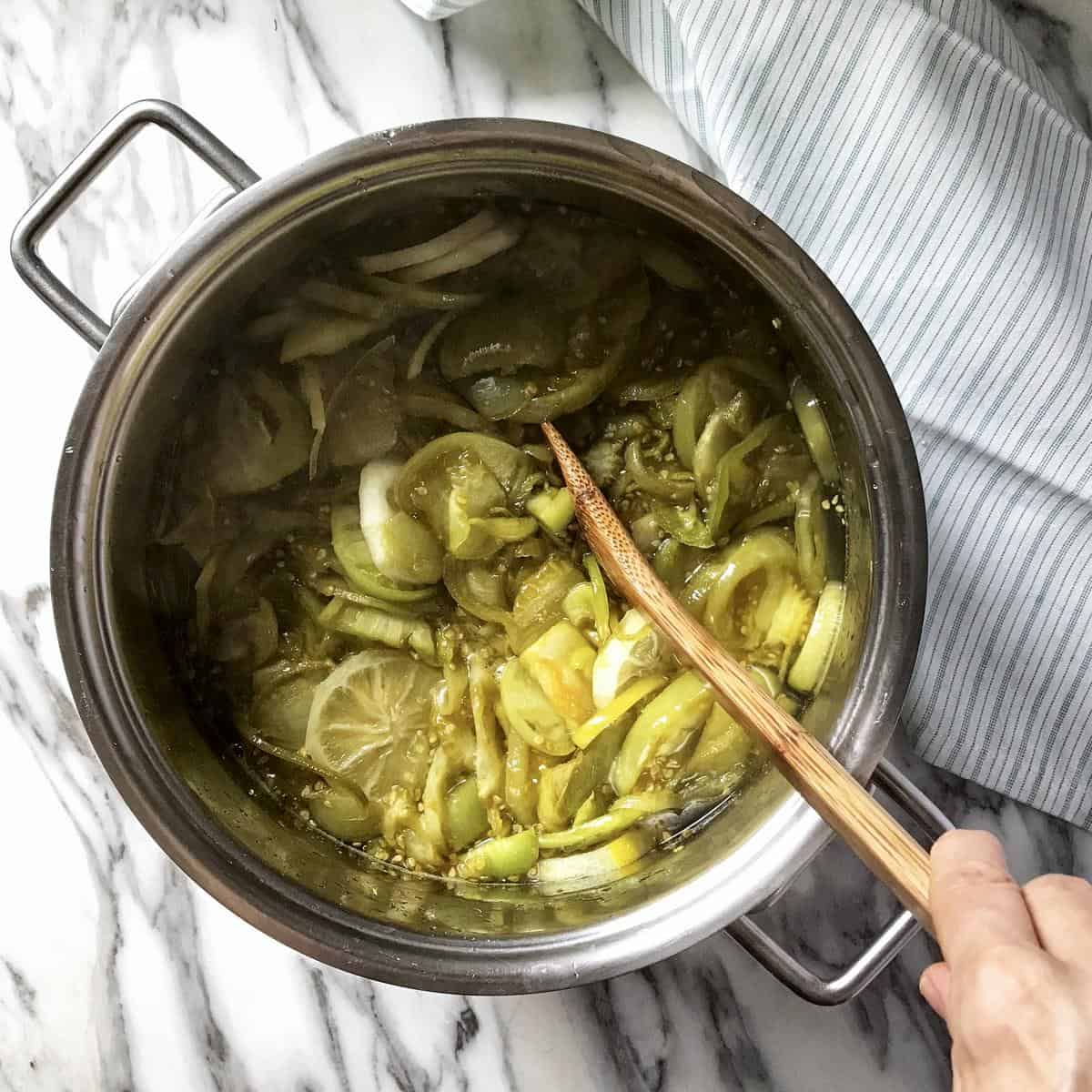 An overhead shot of a pot of green tomato jam in the process of being stirred with a wooden spoon.