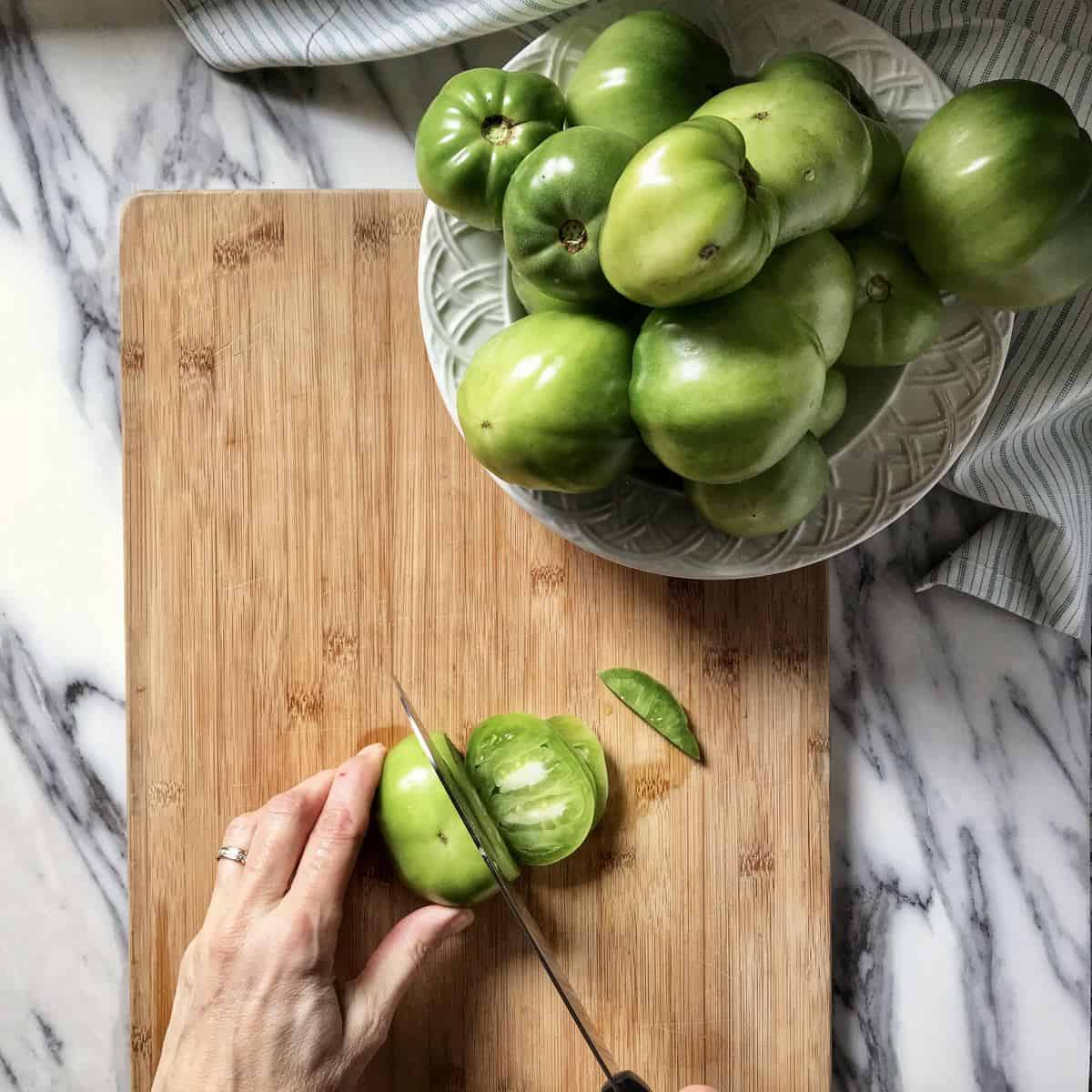 Green tomatoes being sliced on a wooden board to make green tomato jam.