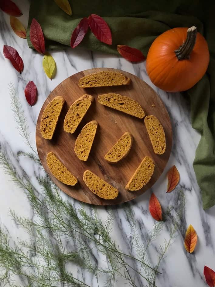 An overhead picture of pumpkin biscotti placed next to a pumpkin and autumn leaves 