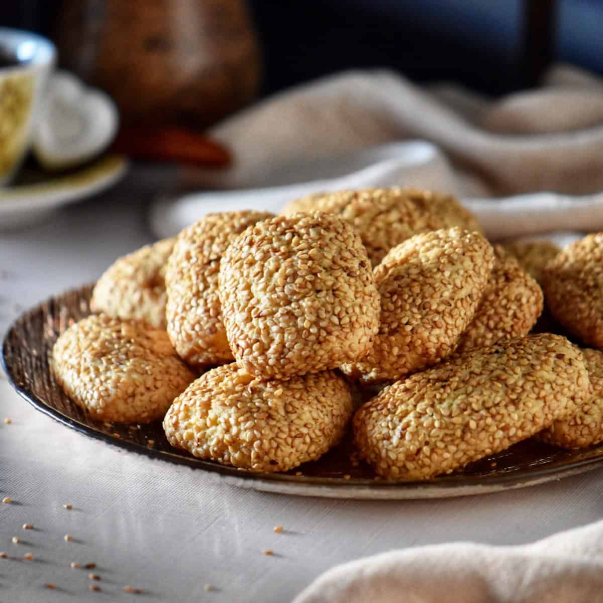 Italian sesame seed cookies on a platter, with a cup of espresso in the background.