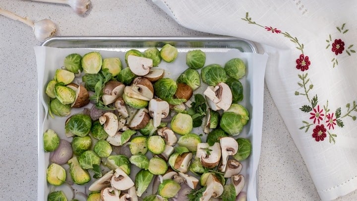 An overhead shot of the mixed vegetables on a large sheet pan, about to be oven roasted.