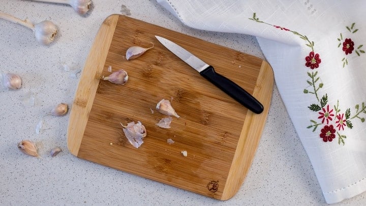 An overhead shot of a few cloves of garlic on a wooden board, getting ready to be oven roasted.