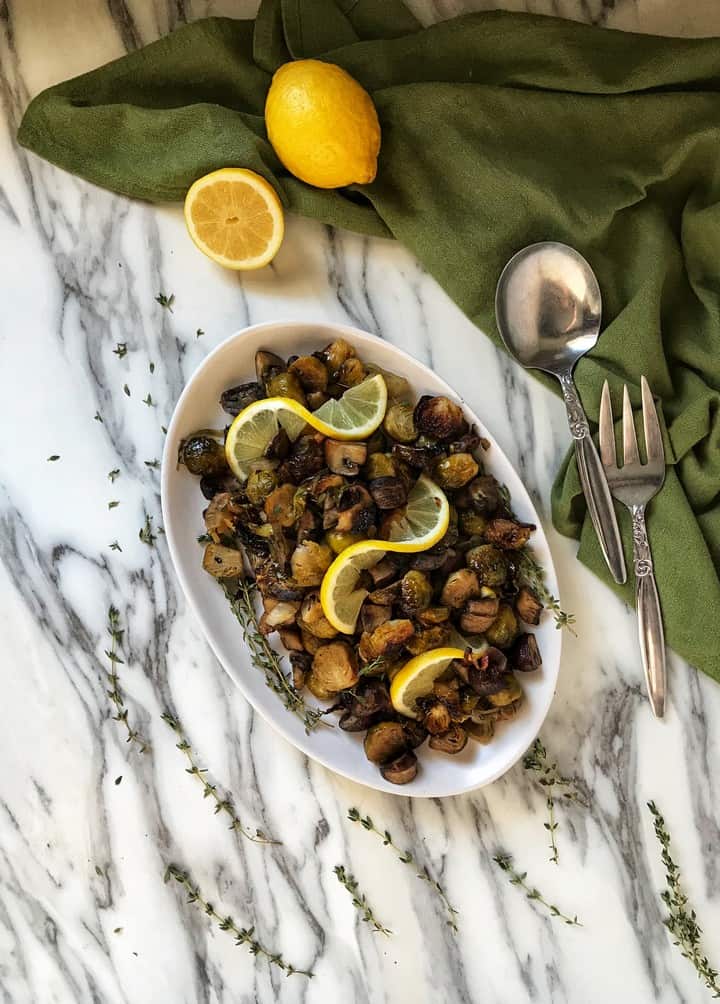 An overhead shot of roasted brussel sprouts, mushrooms, onions and garlic served in a white oval serving tray.