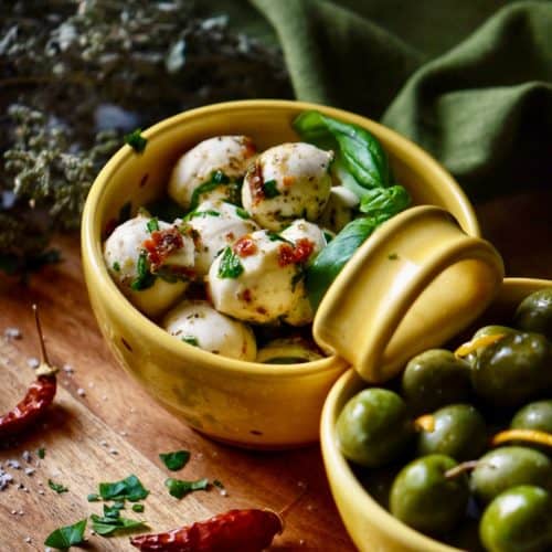 A close up of the marinated mozzarella surrounded with bits of sun dried tomatoes and herbs.